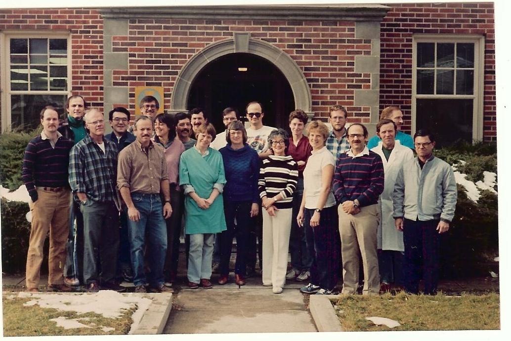 Laboratory of Persistent Viral Diseases group photo, 1987-1988. A large group of men and women on the stairs in front of a brick building.