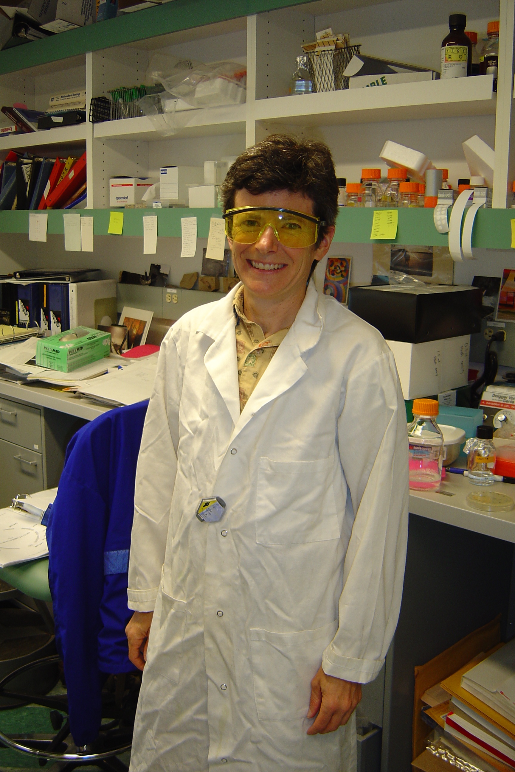 Dr. Kit Tilly in lab, 2004. Wearing safety goggles and smiling.