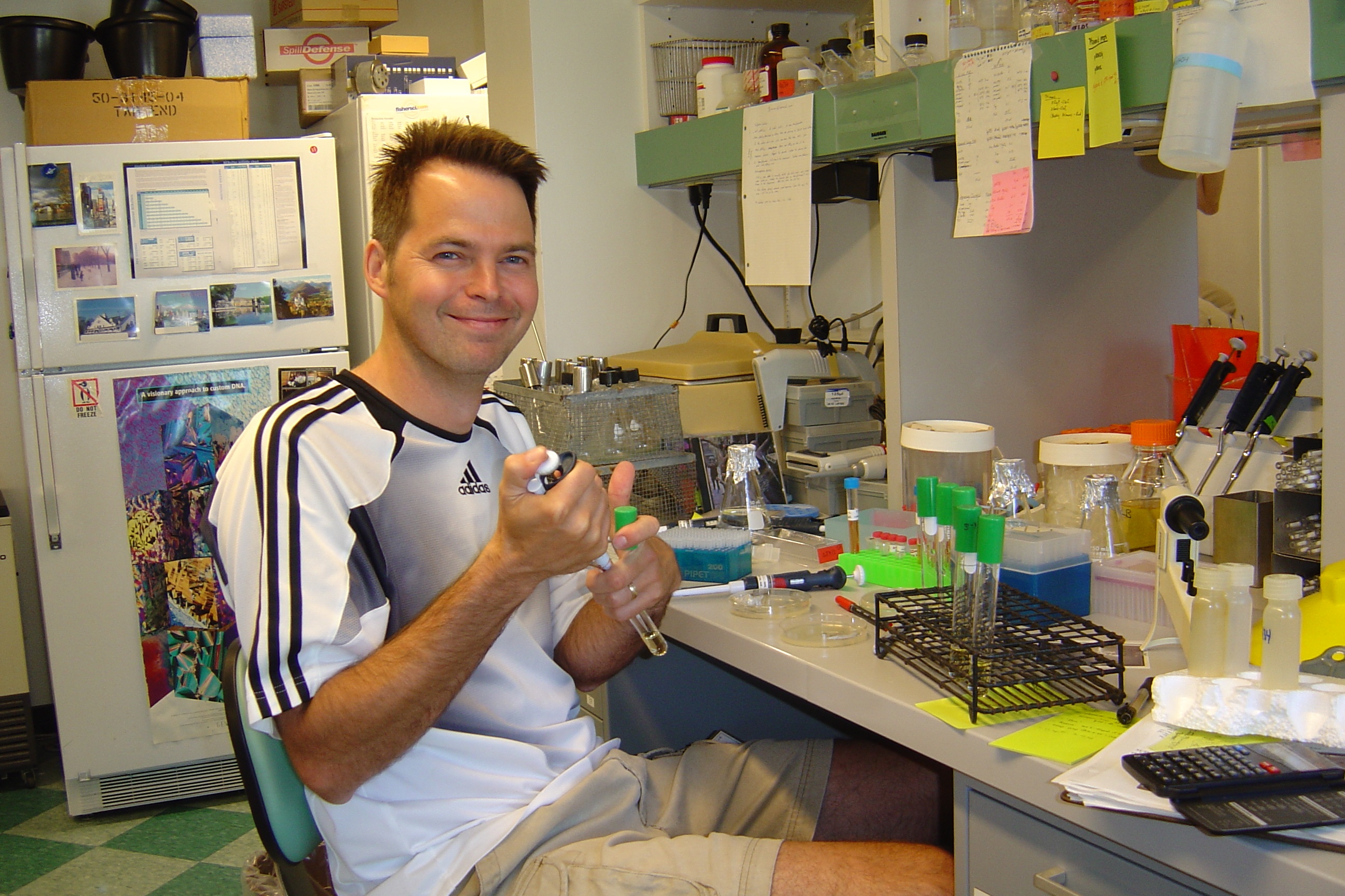 Dr. Phil Stewart in lab, 2004. Smiling while holding a pipette and test tube.