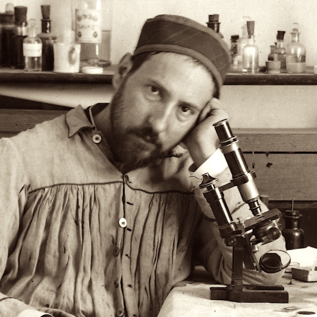 Photograph of Santiago Ramón y Cajal sitting at his drawing table with a microscope printed large on exhibit