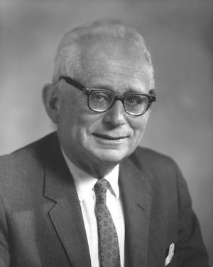 Headshot of DeWitt Stetten from straight on, he is sitting wearing glasses and a suit
