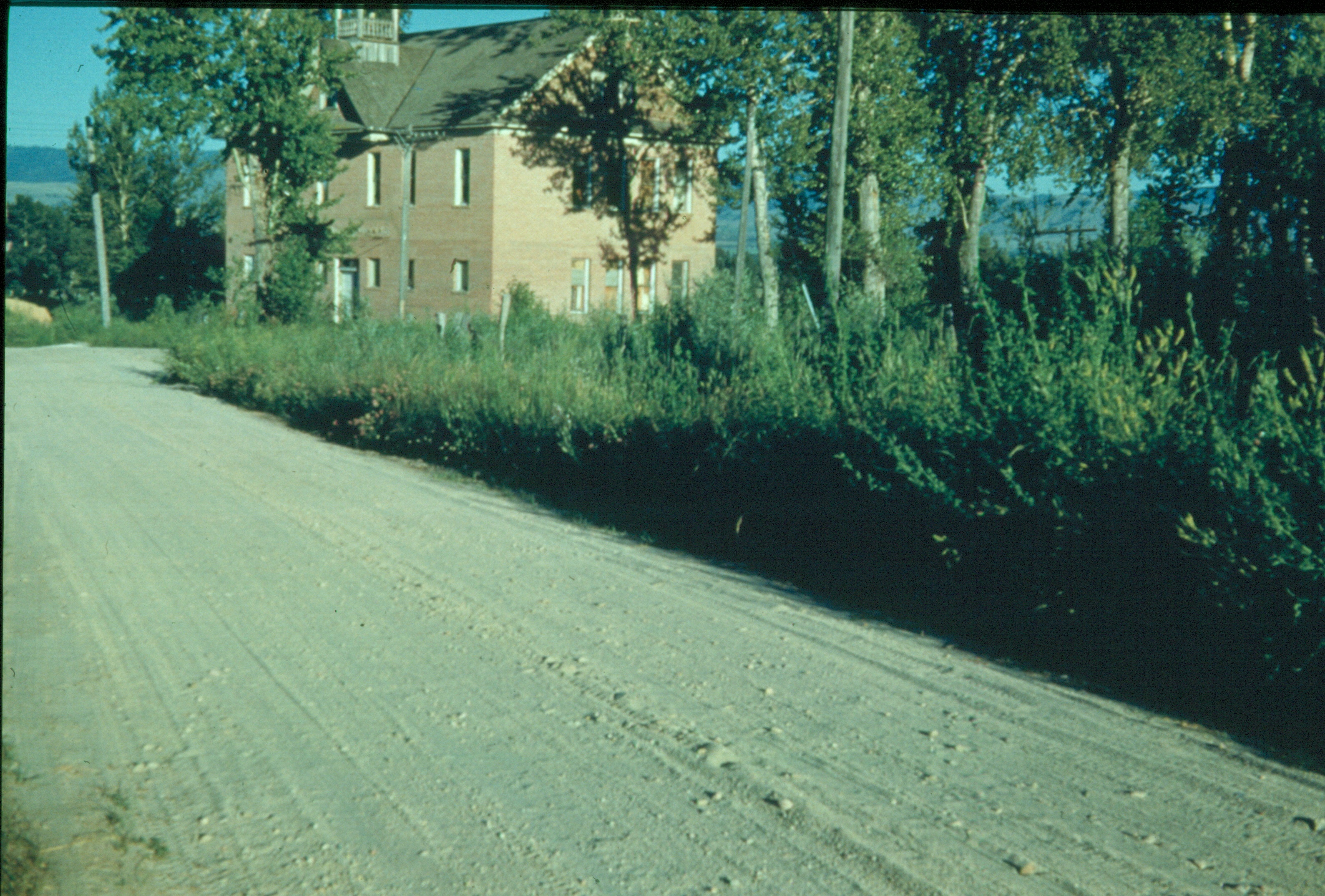 A colorized photo of the Canyon Creek Schoolhouse Laboratory with a dirt road leading past it