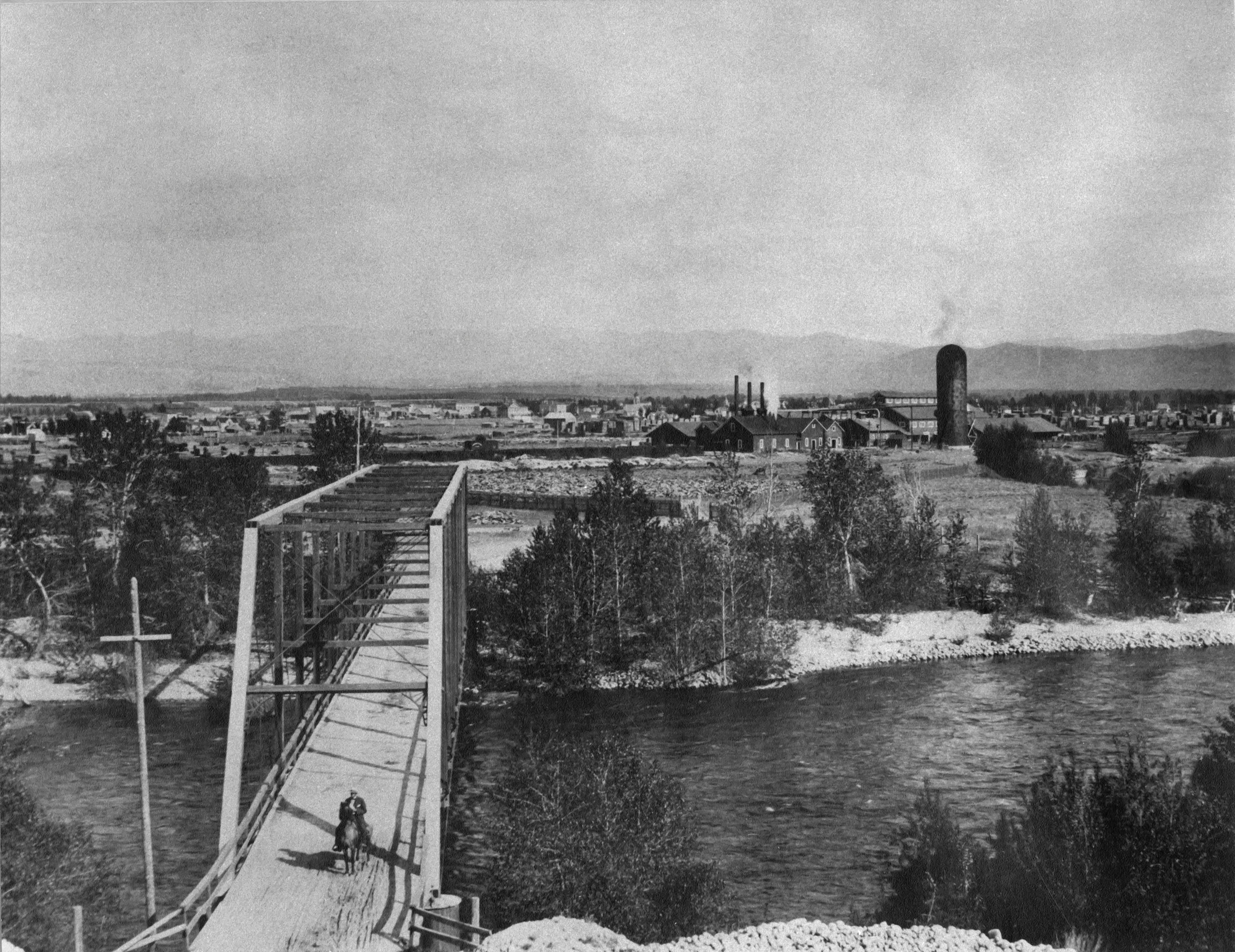 A man rides a horse over a bridge with a town in the background. Taken from some height.