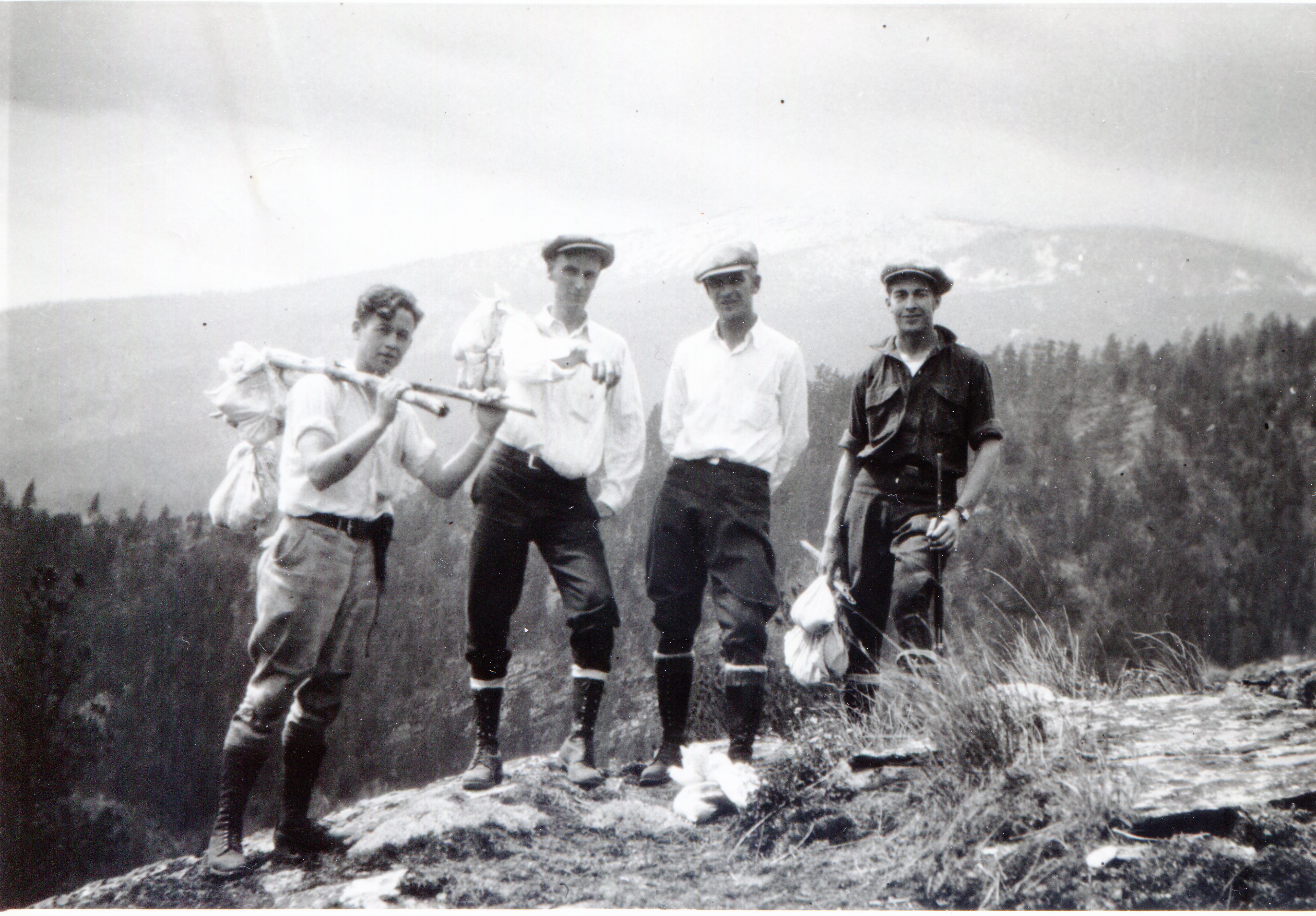 Men pose on top of a mountain ridge, wearing work clothes and carrying tick collecting equipment
