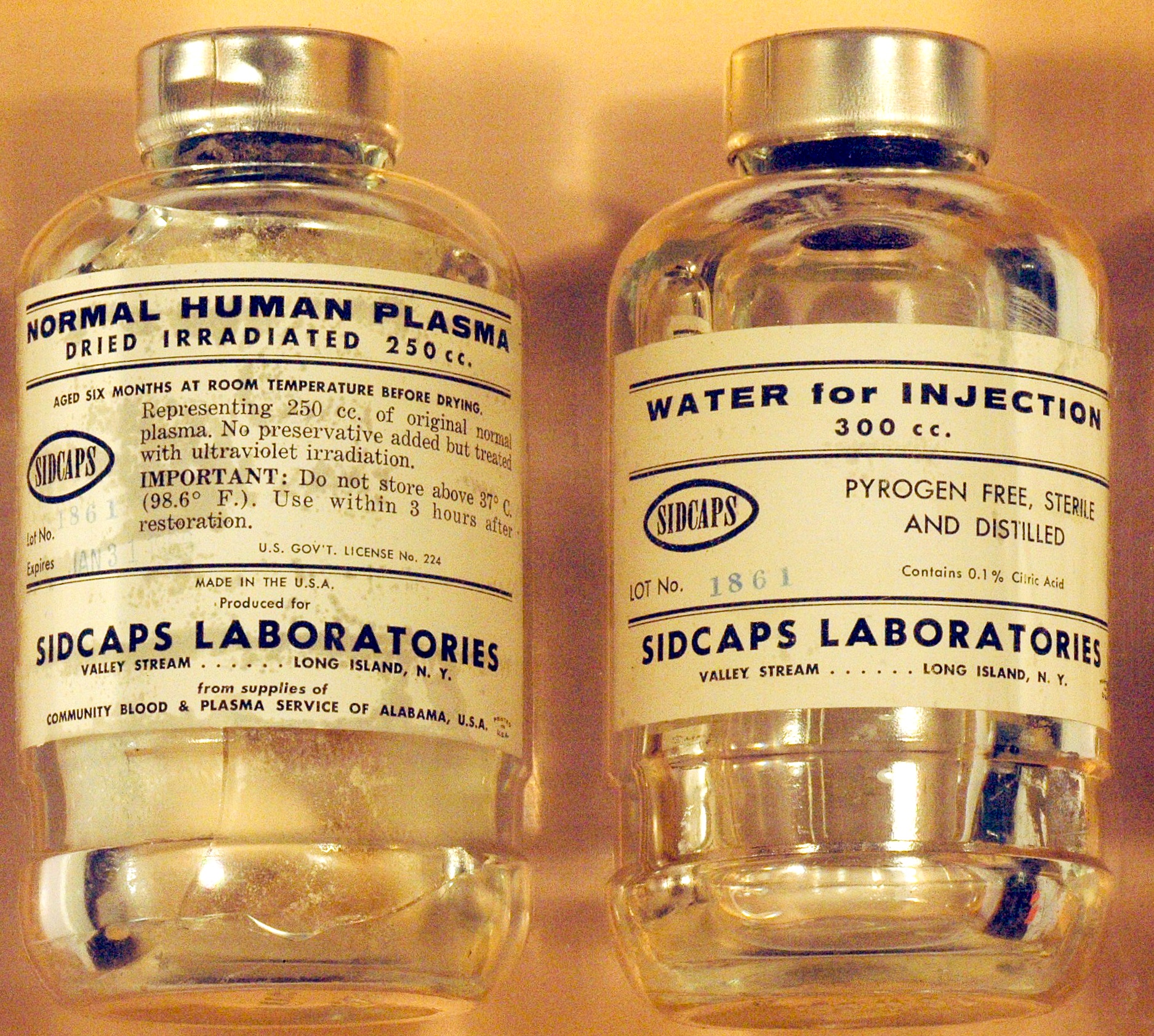 two glass vials, one of human plasma and one of water for injecting. Both from the 1960s, with Sidcaps Laboratories name on them.