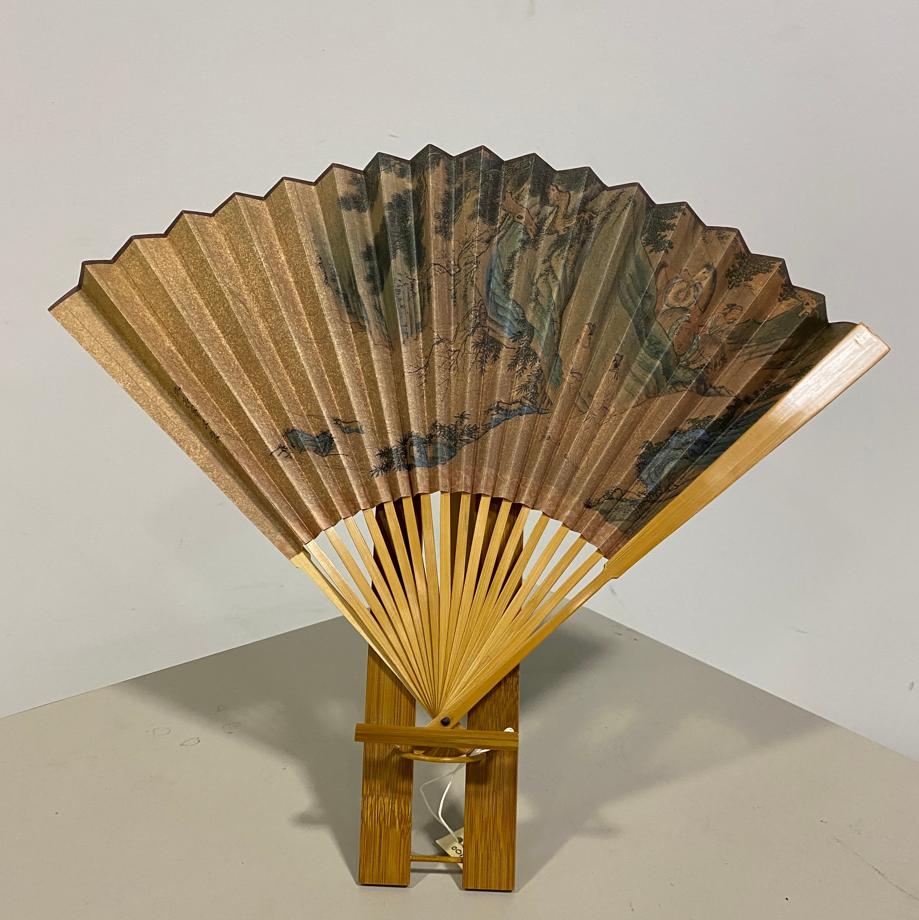 a wooden Japanese fan with mountains, trees, and rivers painted on it