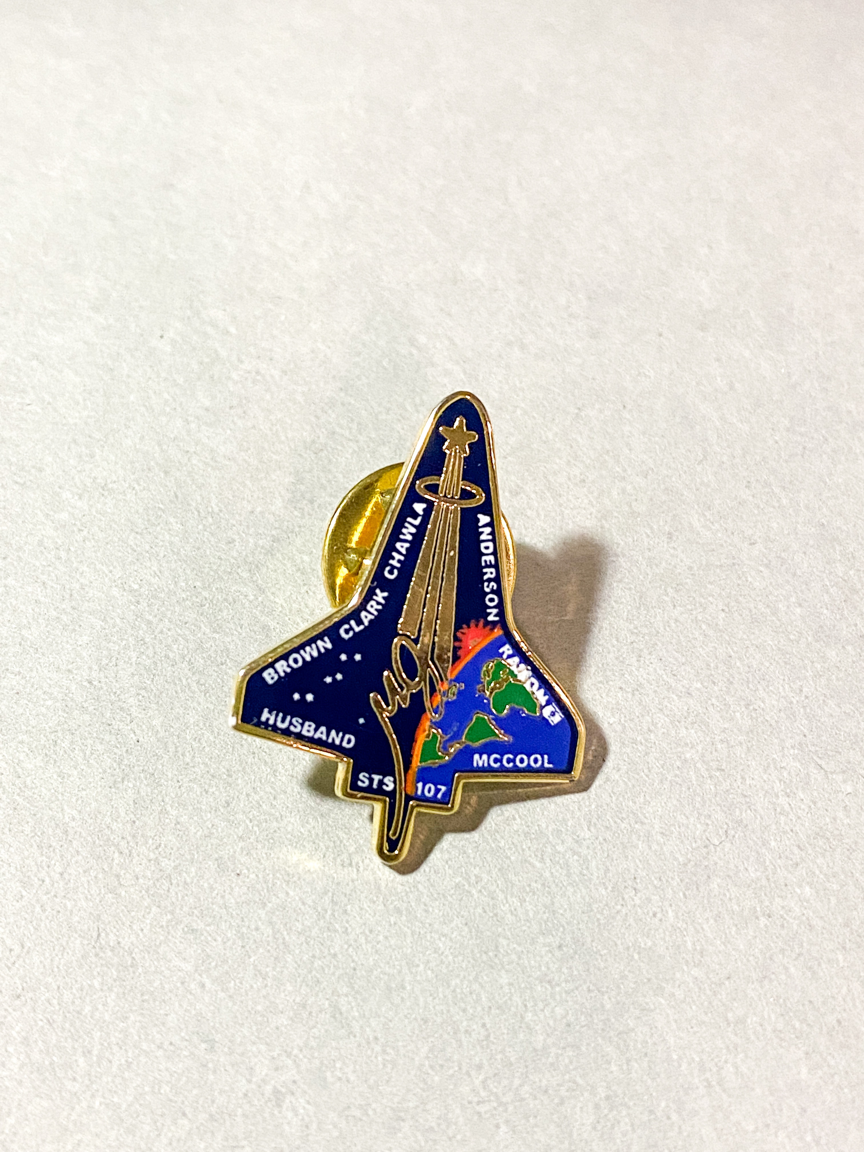 A brass lapel pin shaped like a NASA rocket that belonged to Ruth Kirschstein