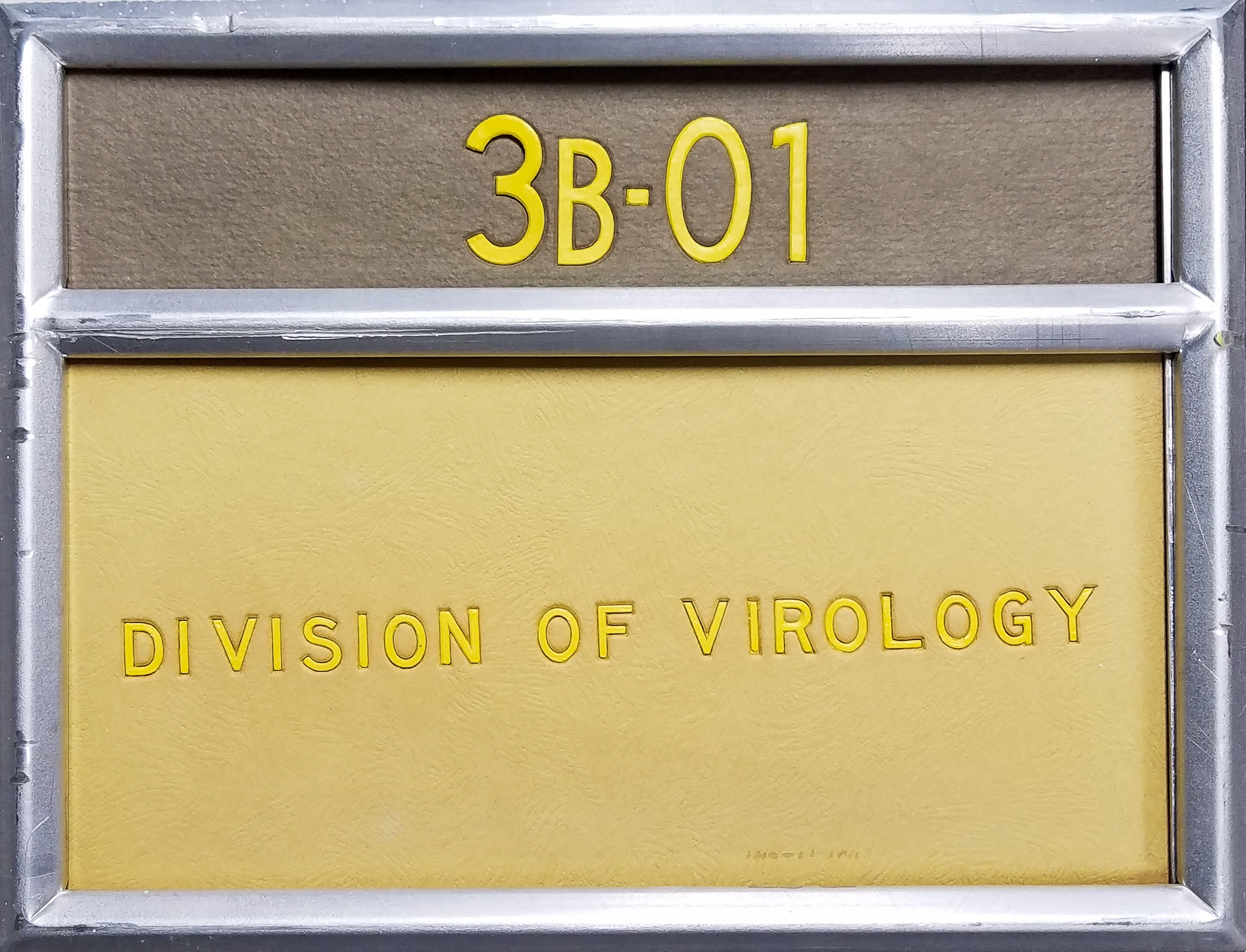 a brown and yellow sign from building 29A for room 3B01, division of virology,  in an aluminum rectangular holder