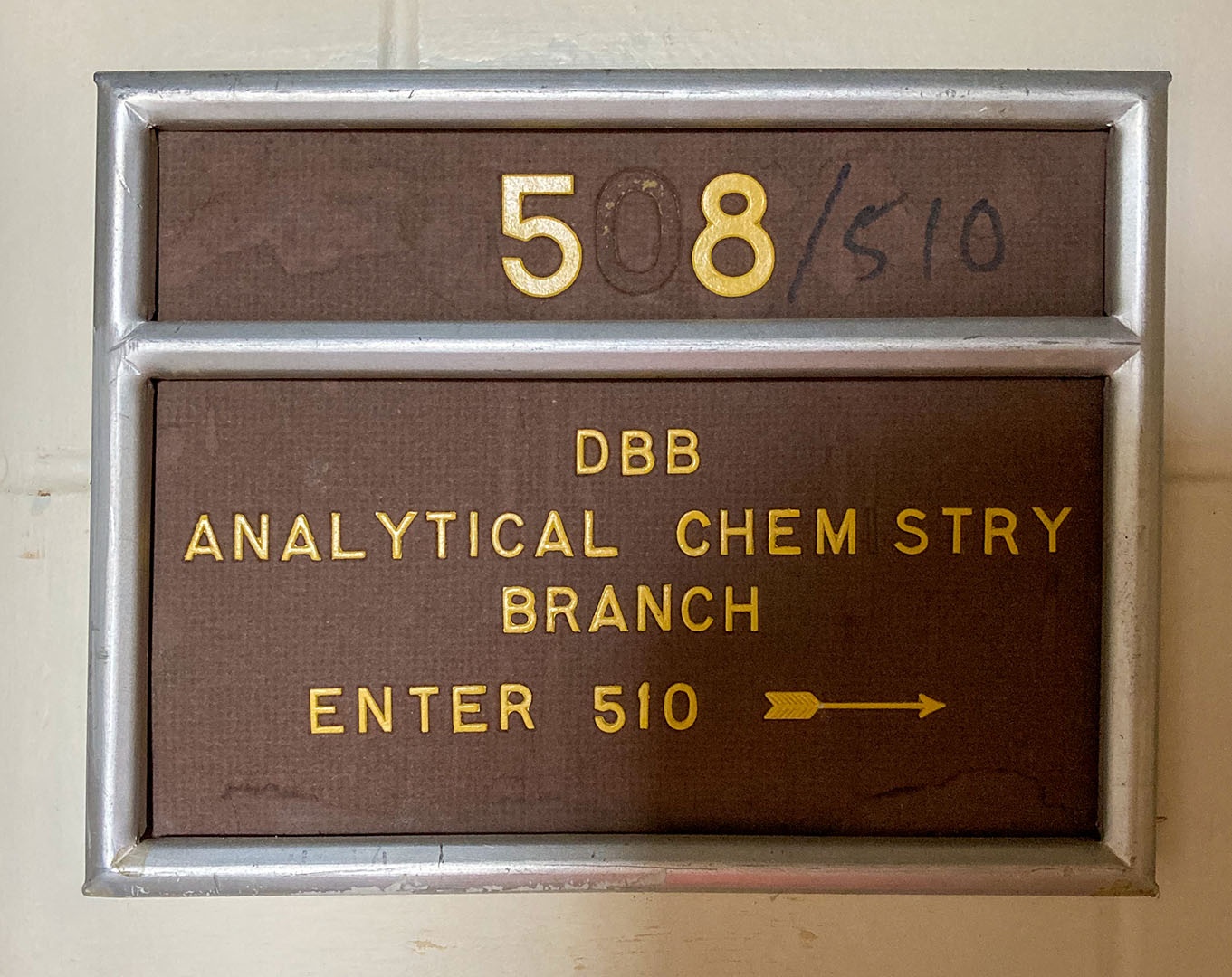 A yellow and brown sign with room number 508 and DBS analytical chemistry branch on it, in an aluminum rectangular holder