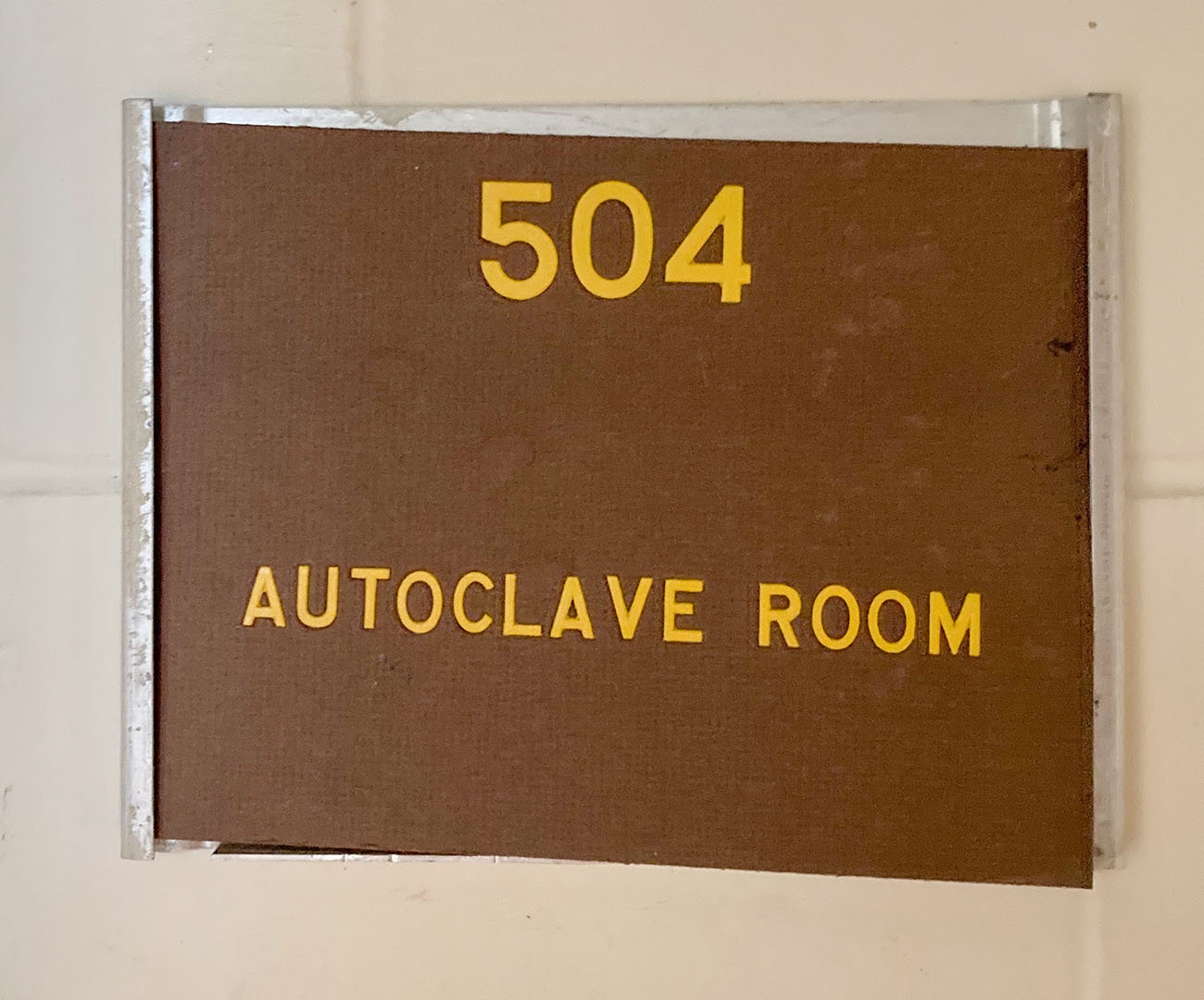 A yellow and brown sign with room number 504 and autoclave room on it, in an aluminum rectangular holder