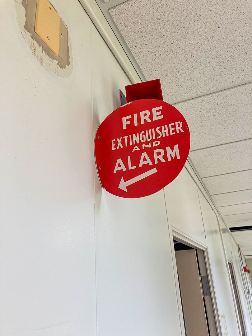 a red circular reflective sign attached to a wall that says fire extinguisher and alarm with a white arrow