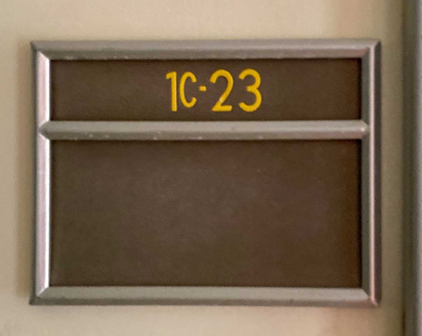 A yellow and brown sign with room number 1C23 on it, in an aluminum rectangular holder
