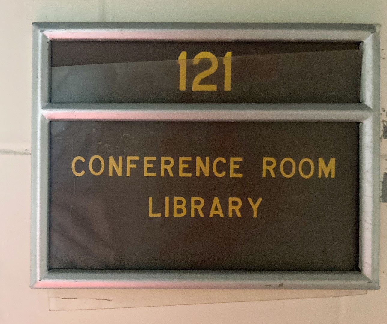 A yellow and brown sign with room number 1C23 on it, in an aluminum rectangular holder