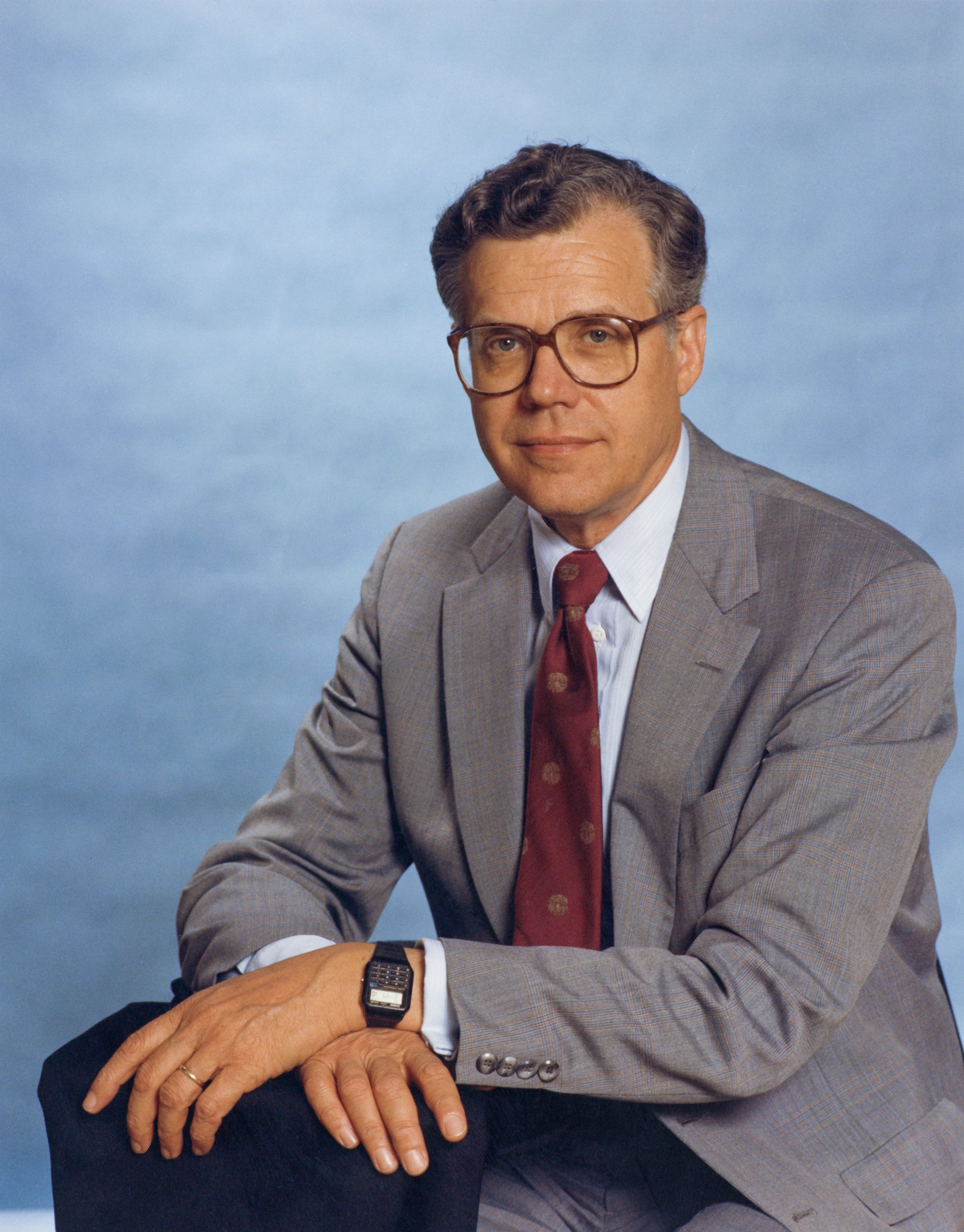 a professional photo of Dr. Paul Parkman in a tan suit with red tie and glasses