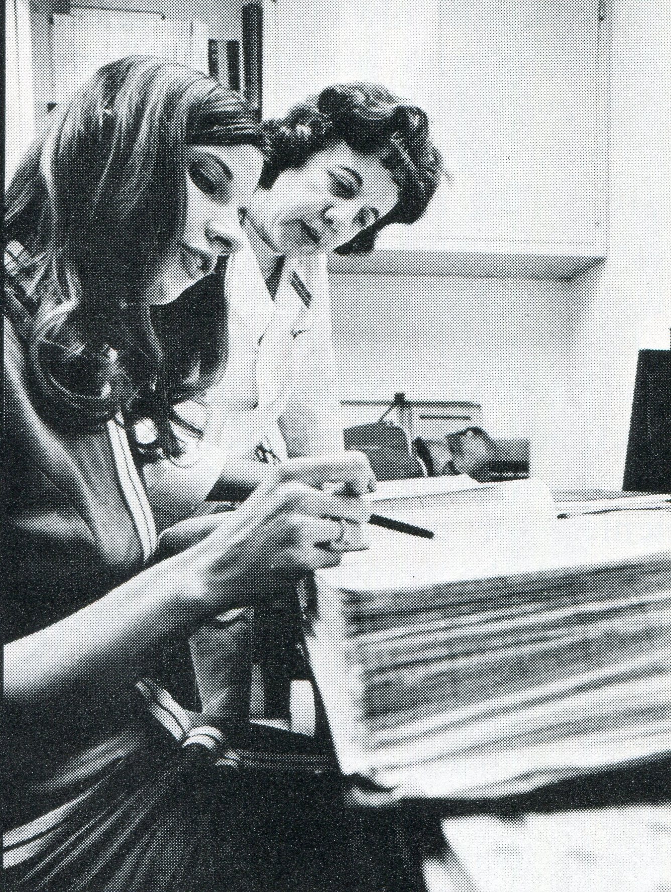 two women, one in a lab coat, look over a book on a table in a blood bank