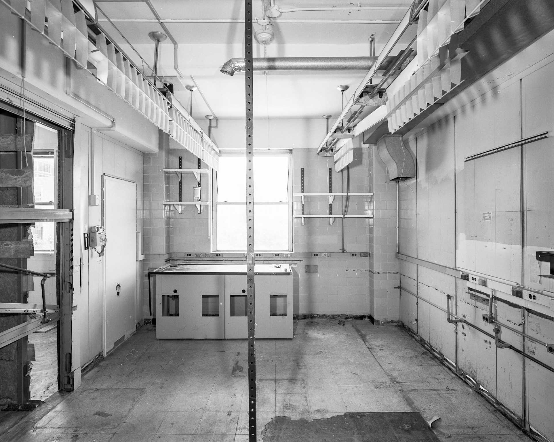 Interior black and white HABS photograph of a lab with an original wall mounted phone,the shelving and cupboards in place taken from the entrance door
