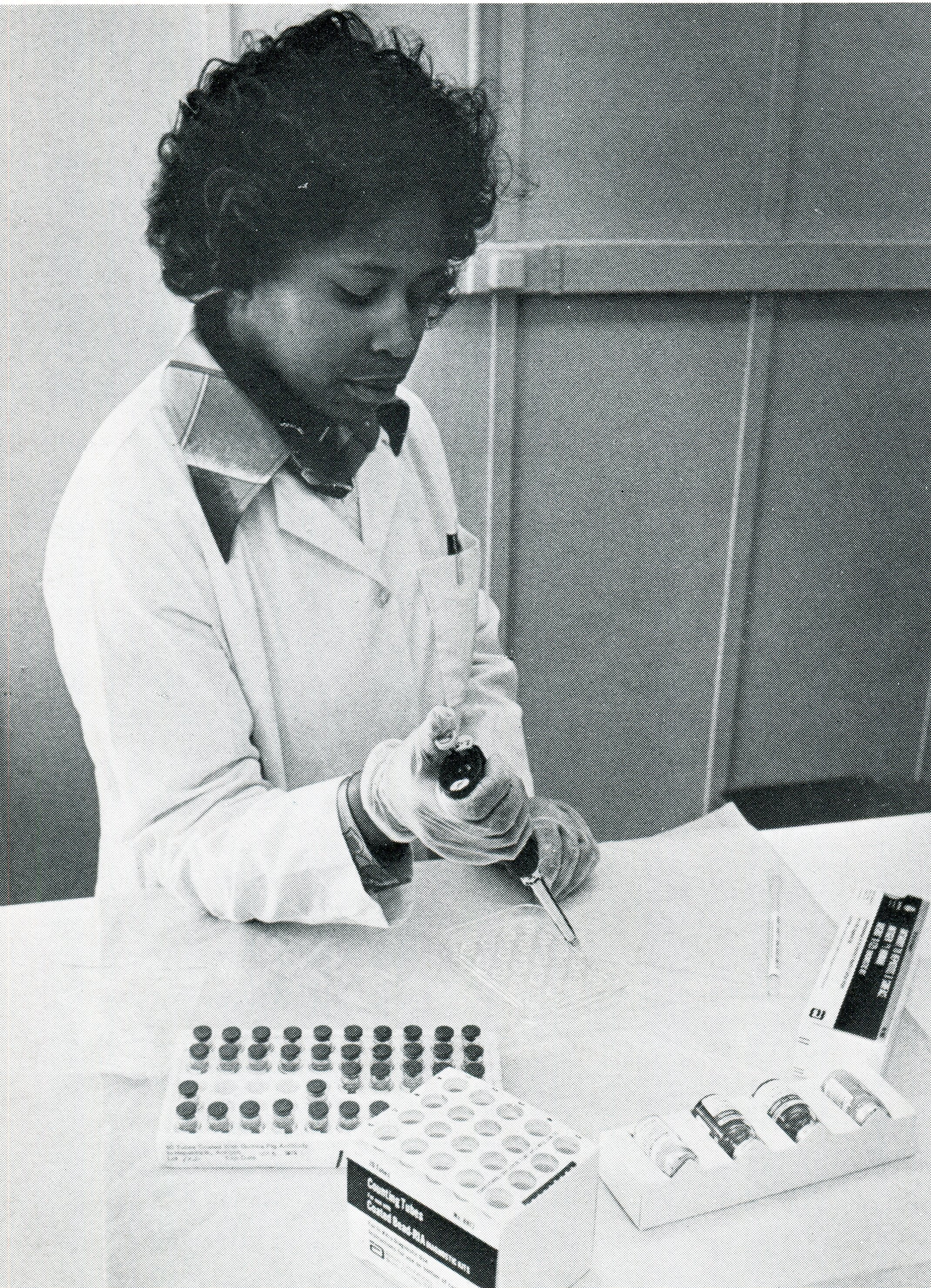 A woman in a white lab coat wearing gloves checks a kit used by blood banks and other facilities to test blood for hepatitis