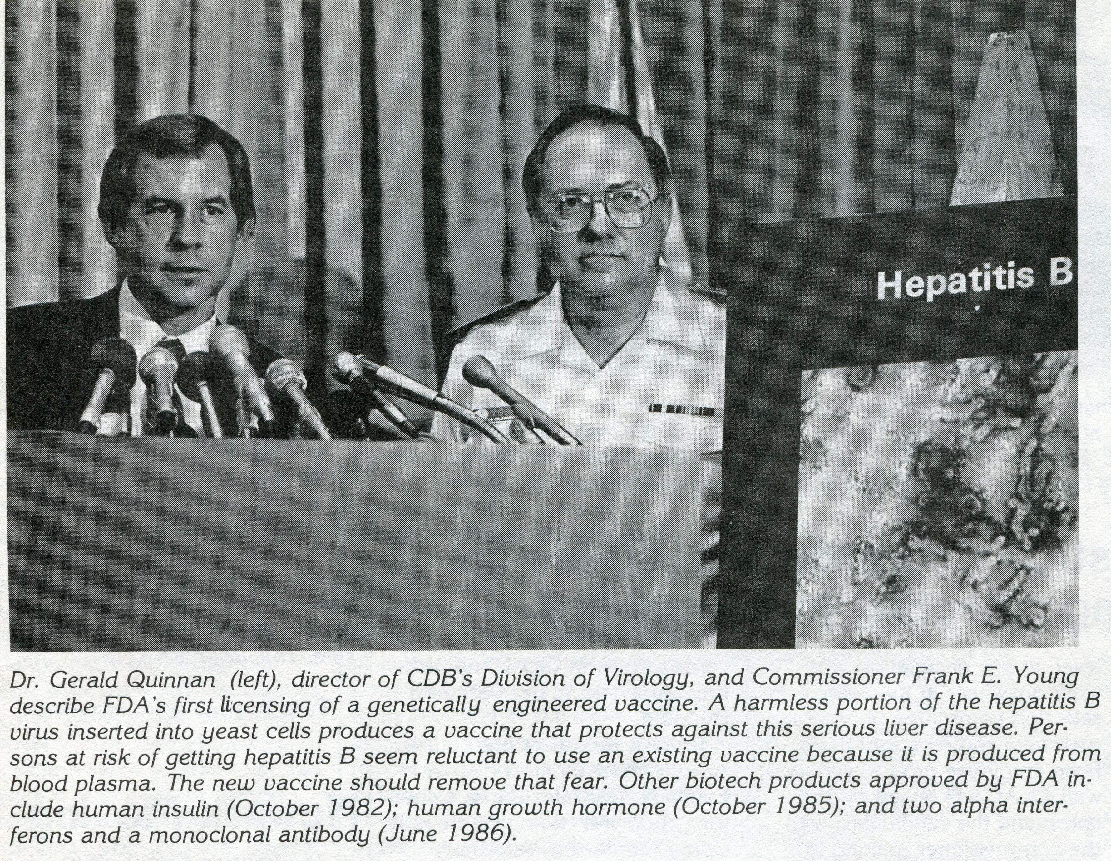 a photo from a newspaper of two men at a press conference, one in uniform and one in coat and tie, with a hepatitis B vaccine poster