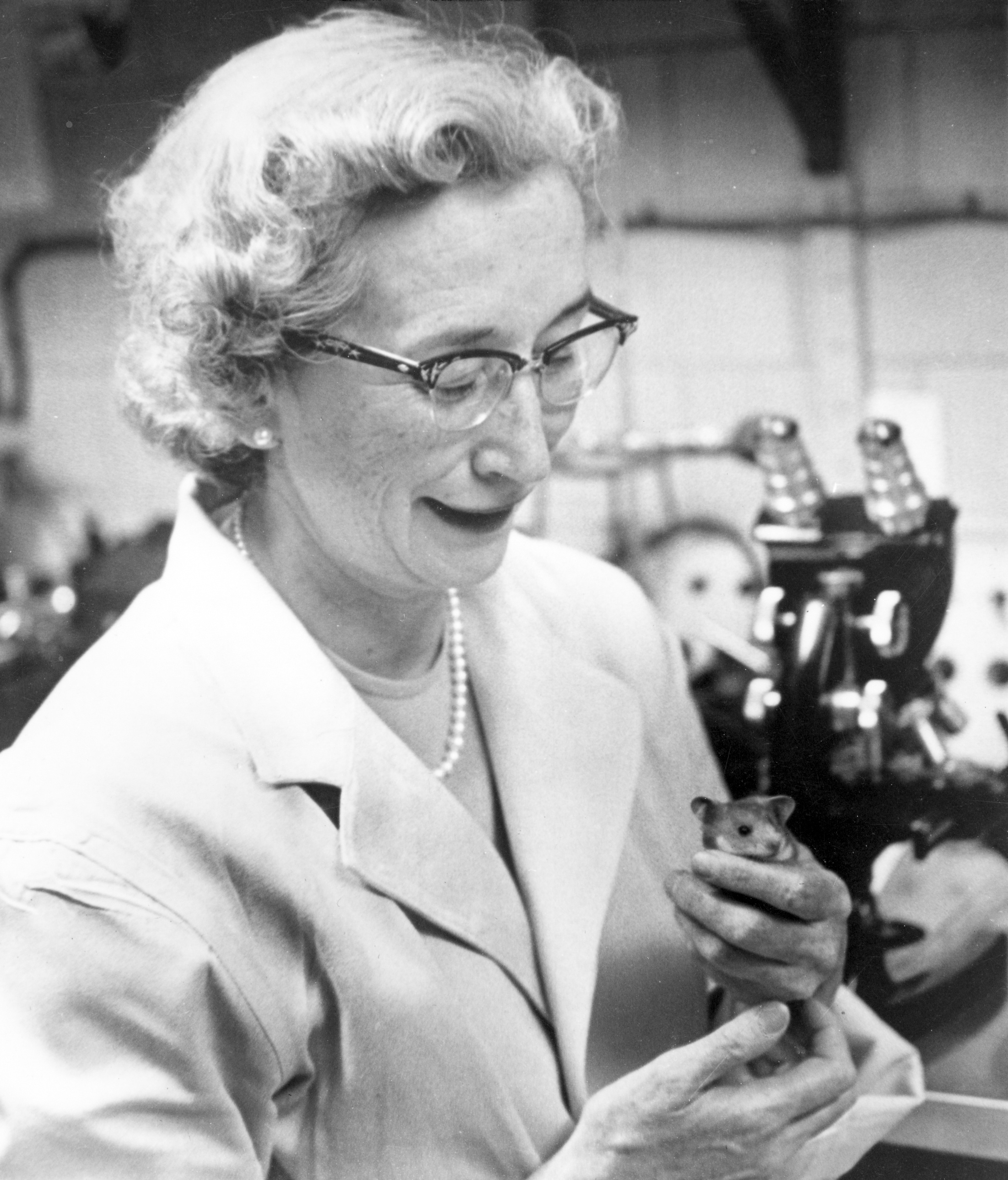 Dr Stewart photographed in the lab, holding a mouse and smiling.