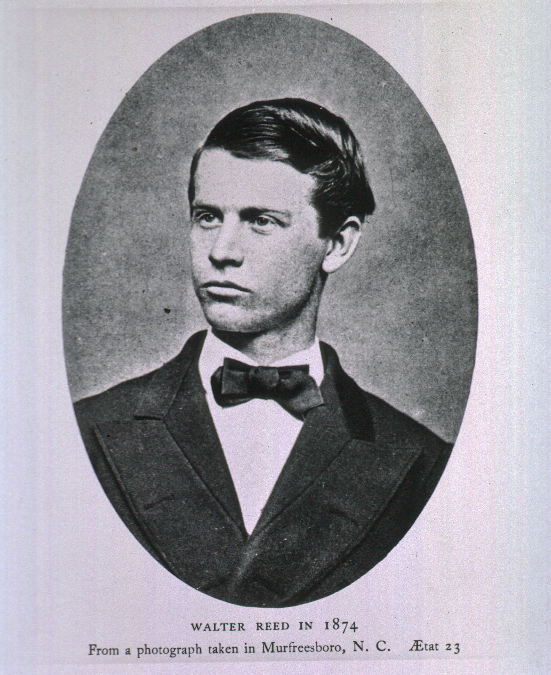 black and white photograph of Walter Reed in 1874 in Murfreesboro, North Carolina. He is a young looking man with short hair, wearing a black bowtie and white collared shirt.