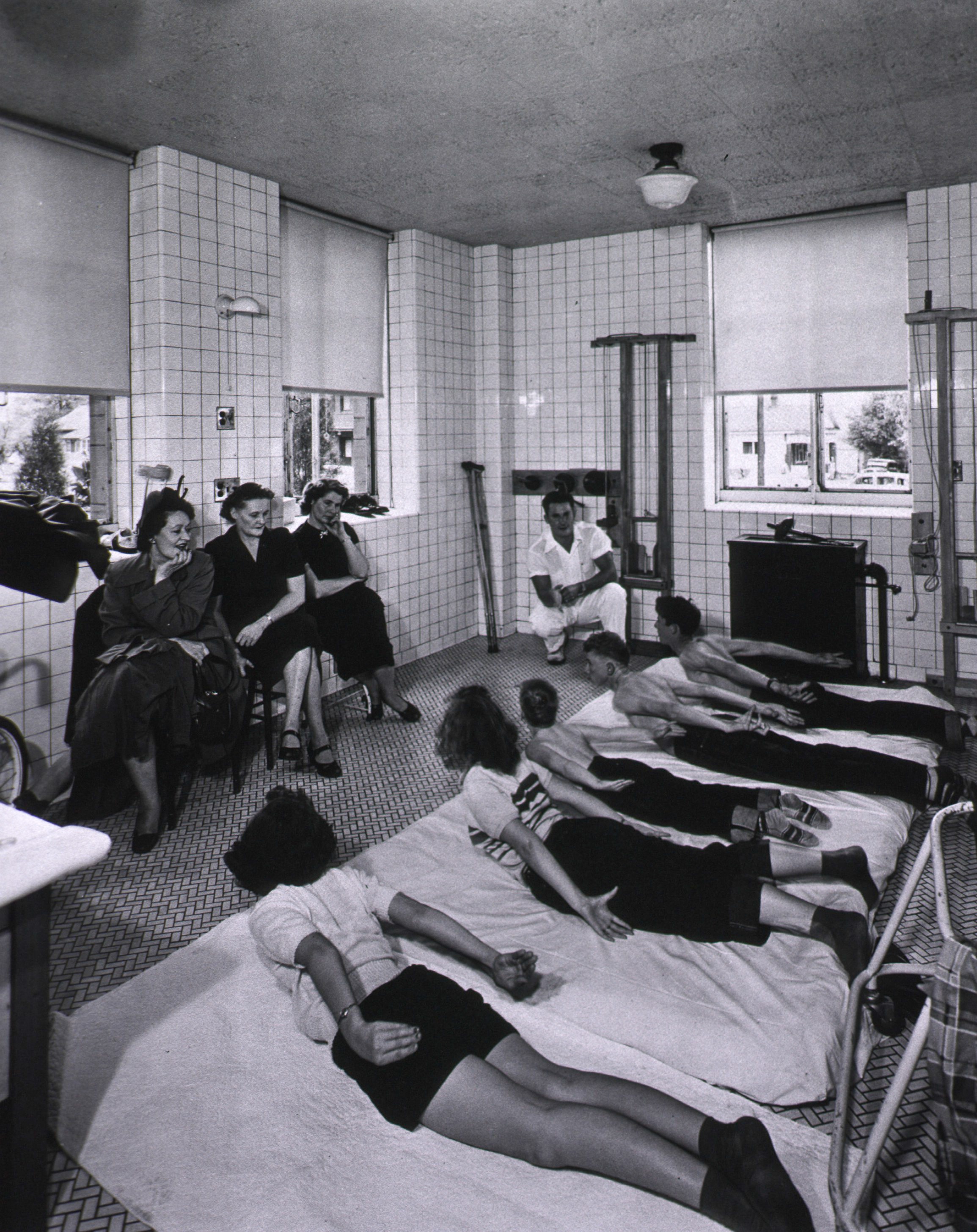 Photo of a physiotherapist giving directions to convalescent pediatric polio patients with mothers watching