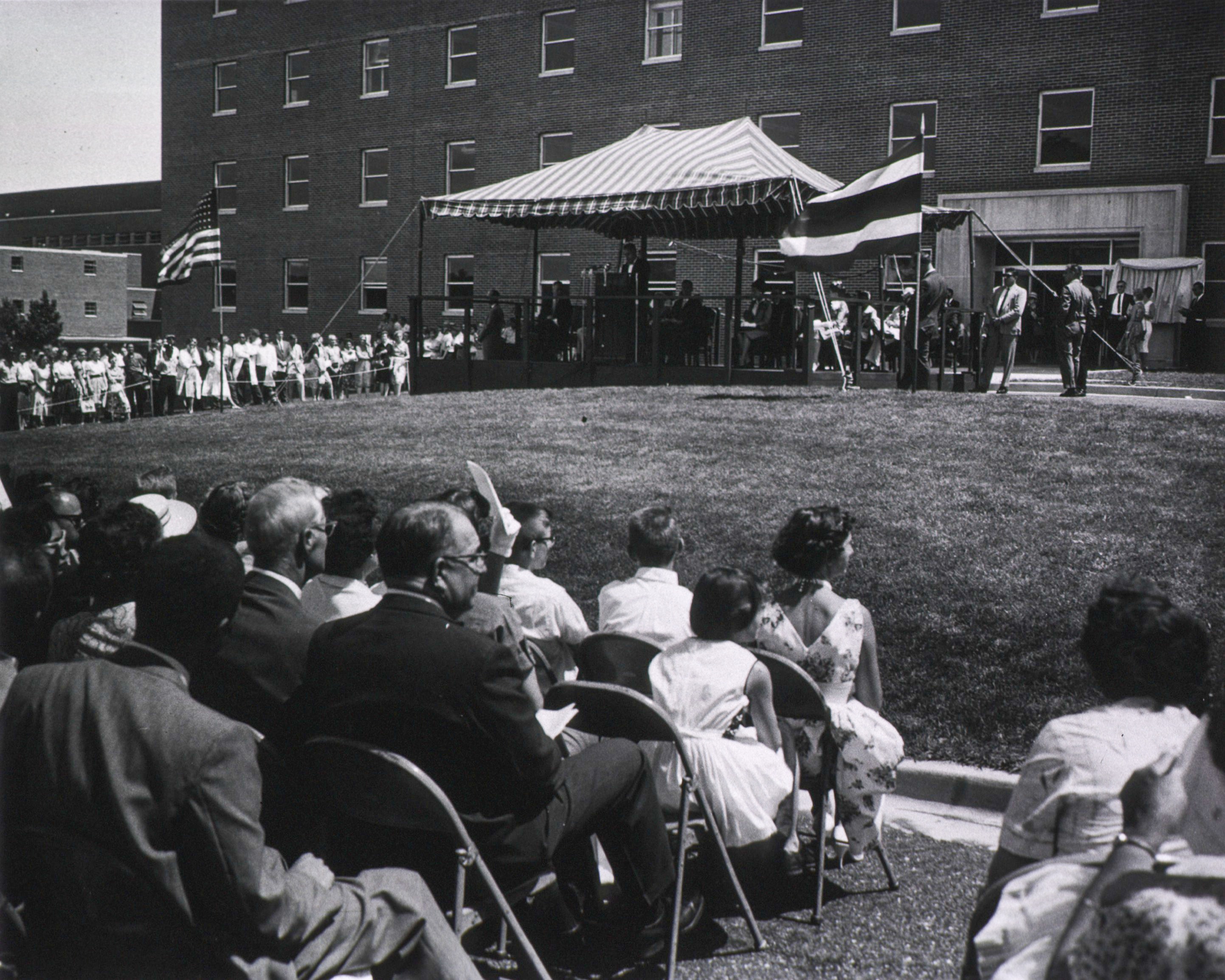Building 29 Dedication Ceremony with people sitting in chairs on the lawn and speakers under a tent by the main entrance in 1960