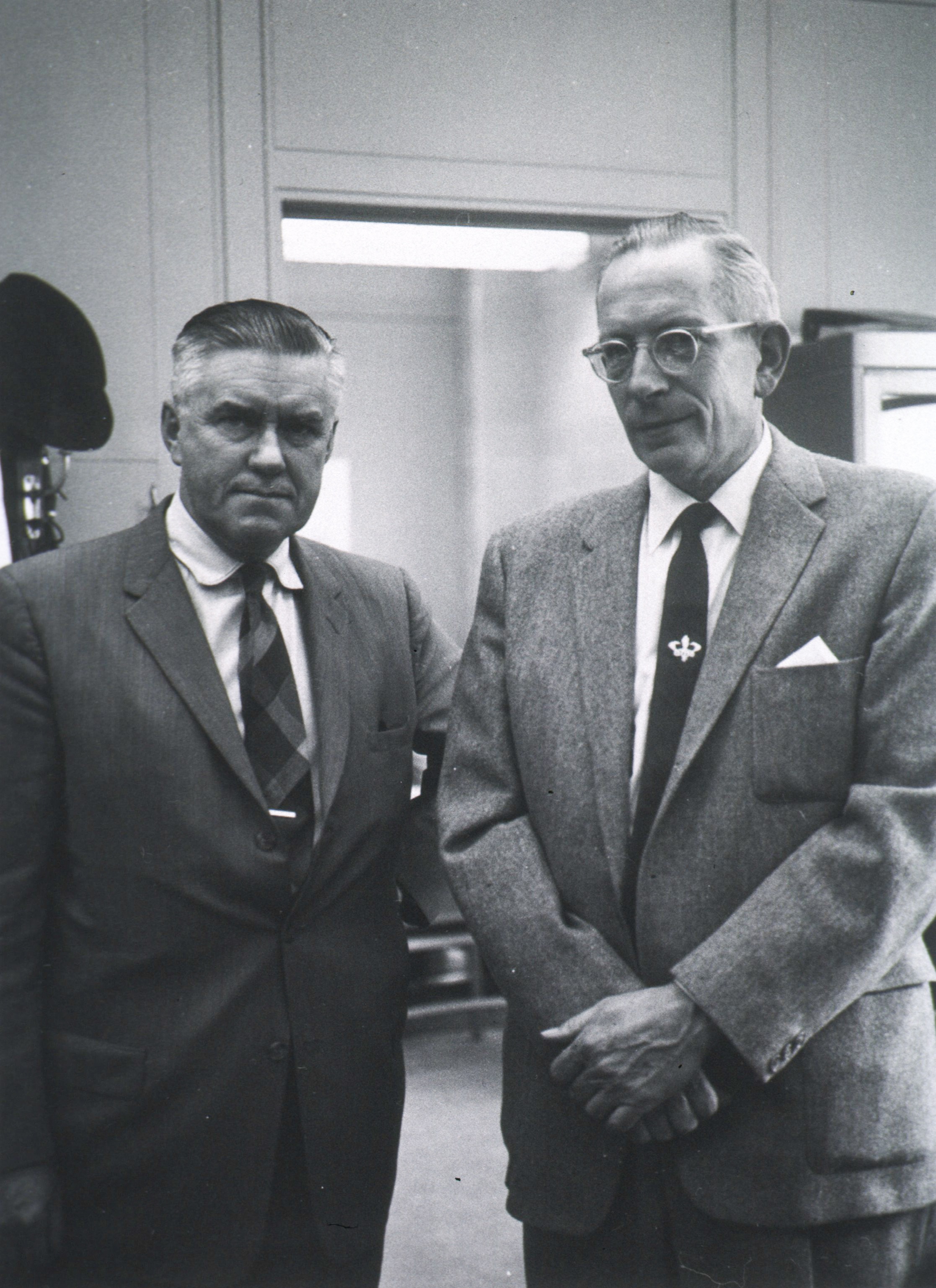 two older men in suits, stand for their photo to be taken.