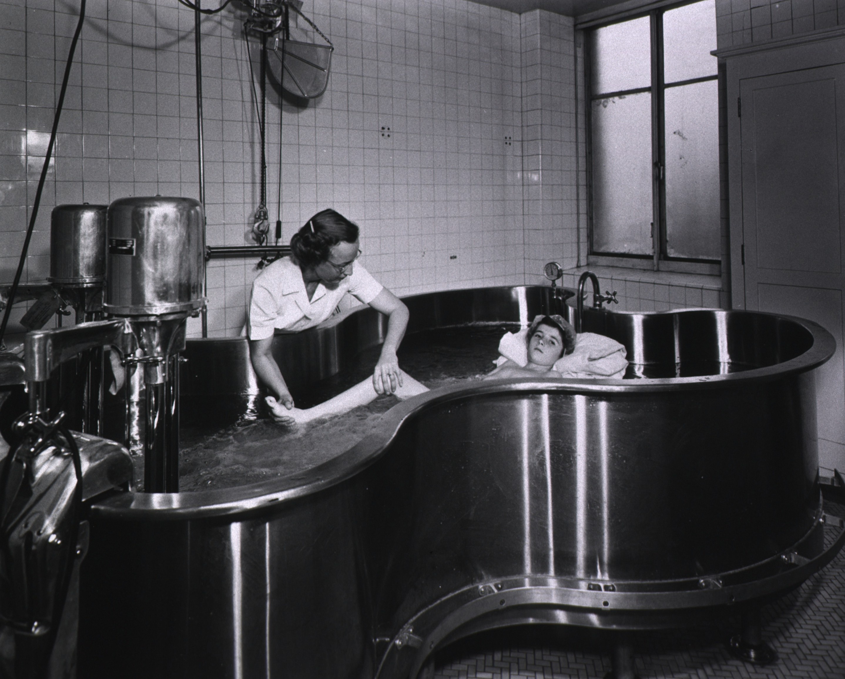 A polio patient in a large whirlpool tub is receiving treatment