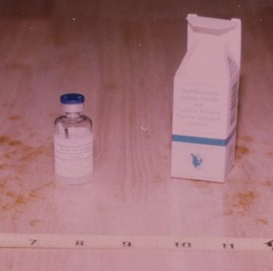 A vial of tetanus antitoxin and the dried antiserum are held up in someone's hands.