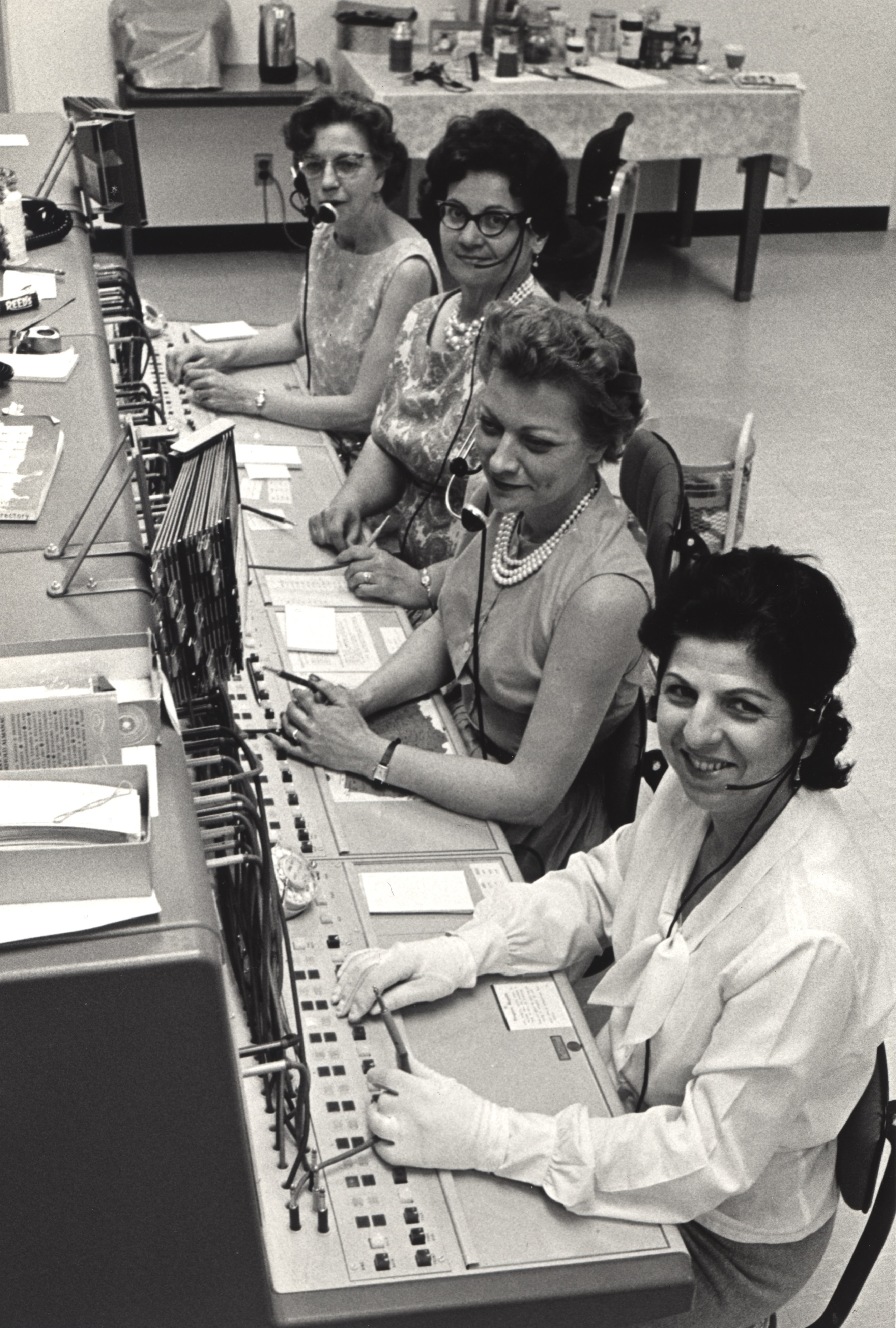 Four women sit at the NIH telephone operator exchange, looking at photographer, c. 1953
