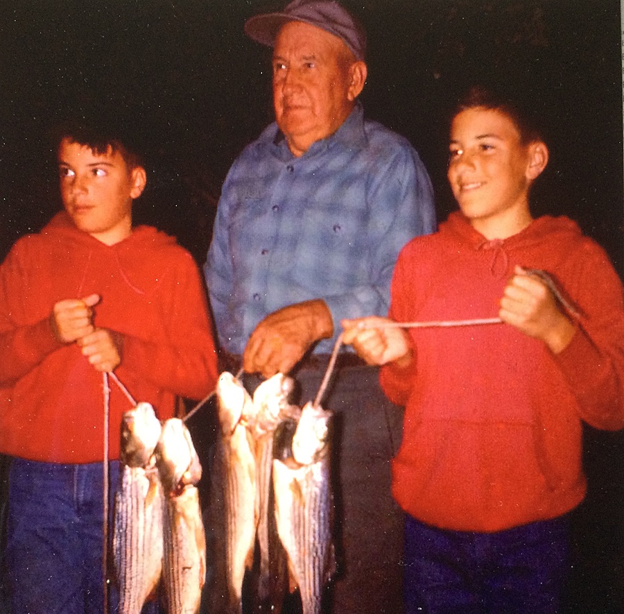 An older man holding a fish on a line with a boy on either side doing the same.