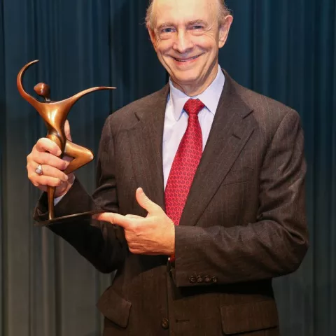 A man wearing a suit and tie holds an award in his hand.